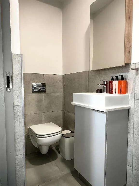 Modern bathroom with wall-mounted toilet, white vanity sink, gray tile walls