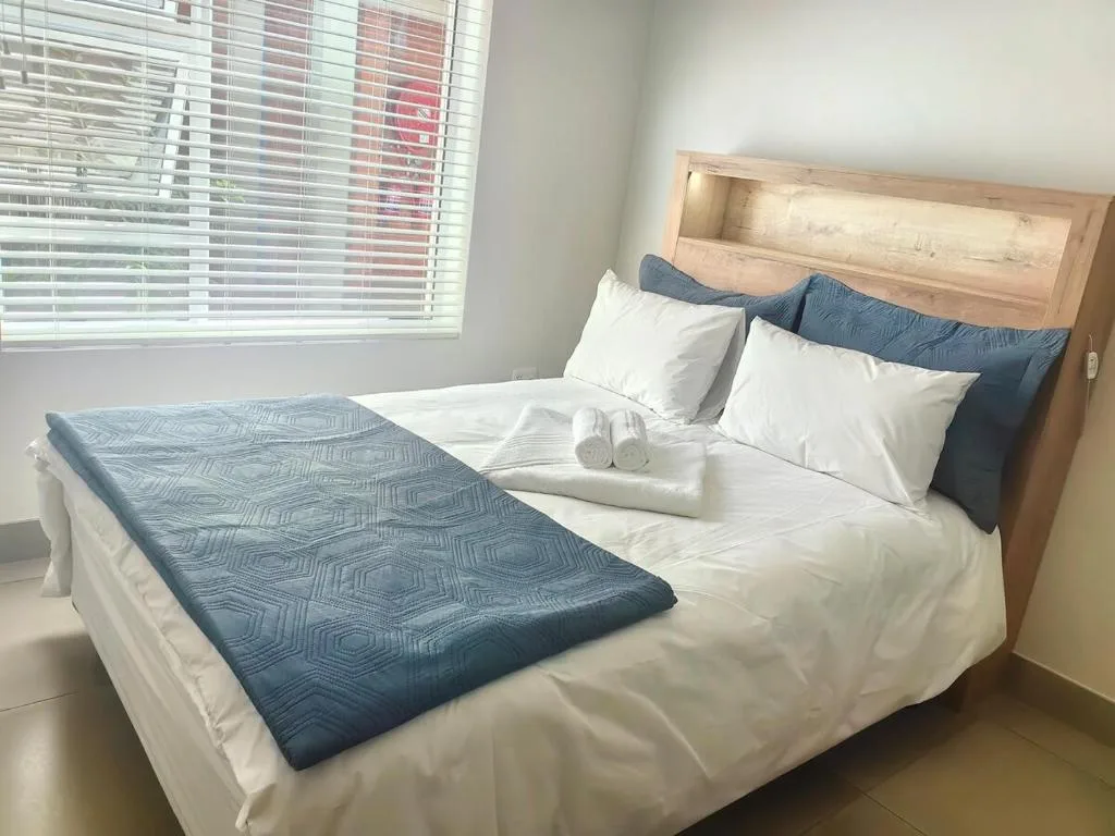 Spacious bedroom with wooden bed frame, white linens, and blue patterned throw
