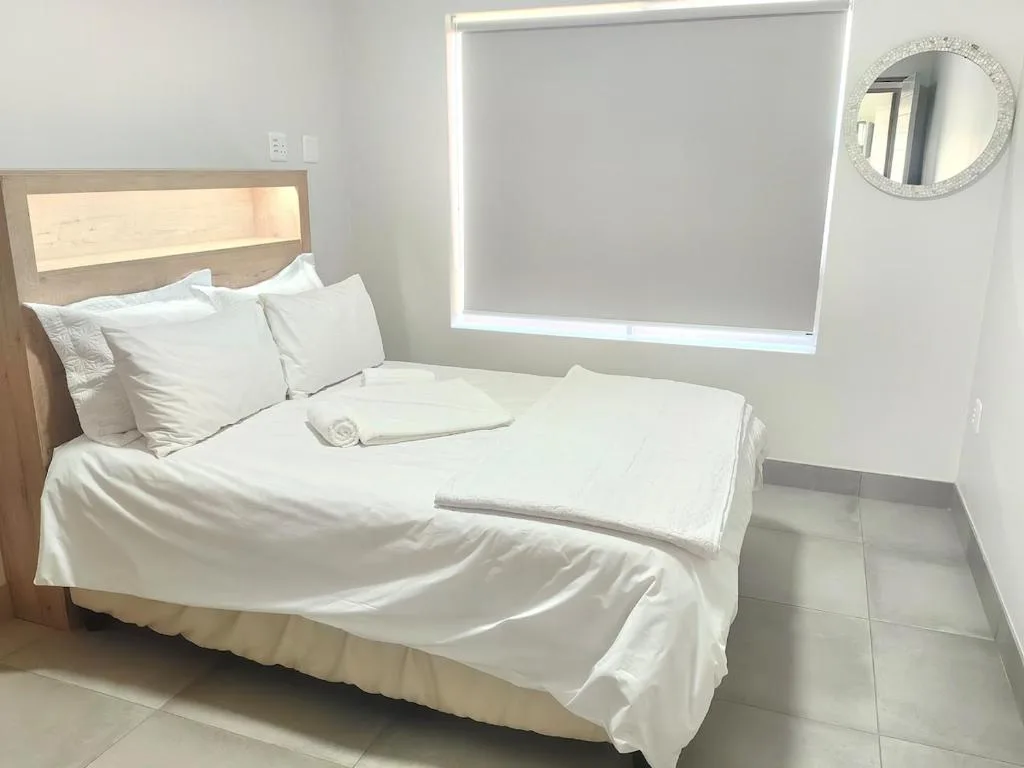 Clean bedroom with white bedding, wooden headboard, and bright window