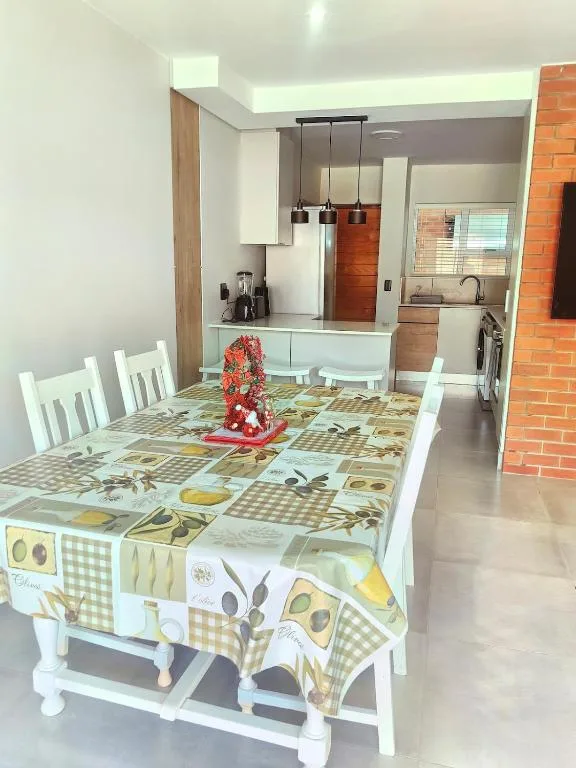 Dining table with patterned tablecloth and white chairs, kitchen visible beyond