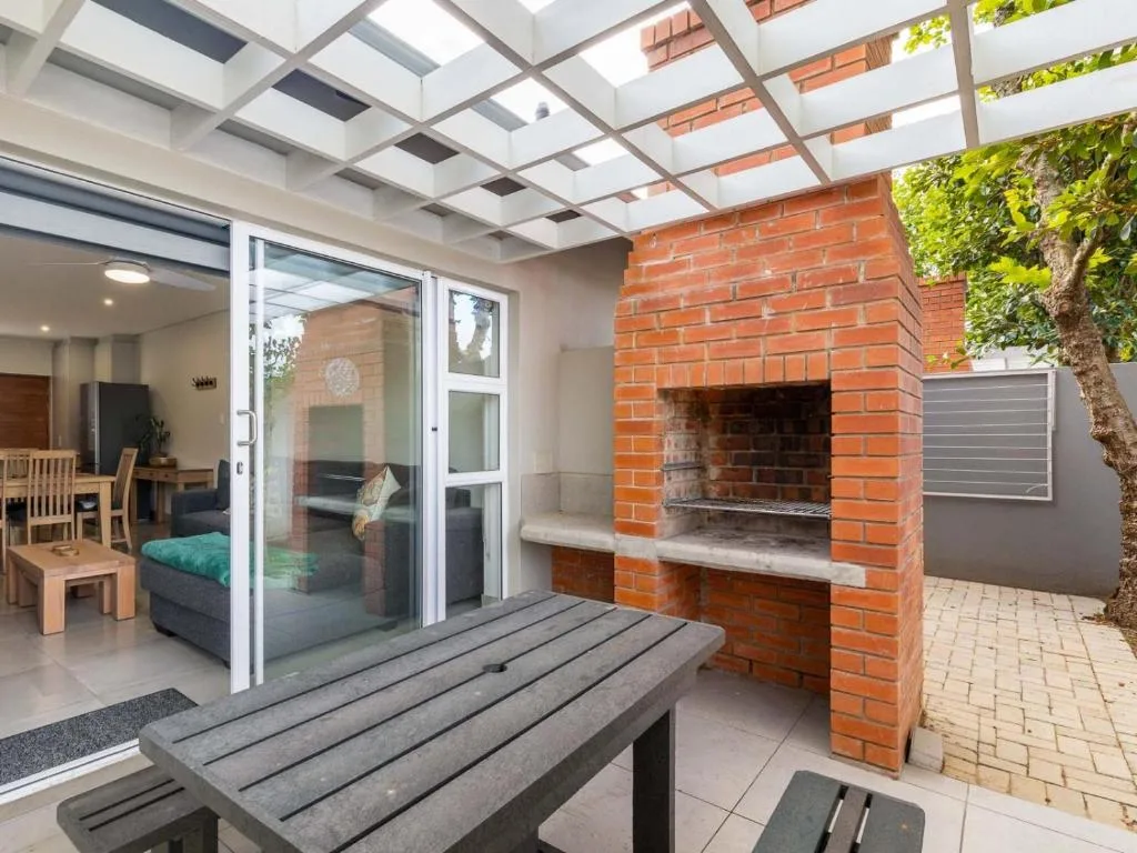 Covered patio with built-in brick braai, wooden bench seating, and glass doors opening to interior