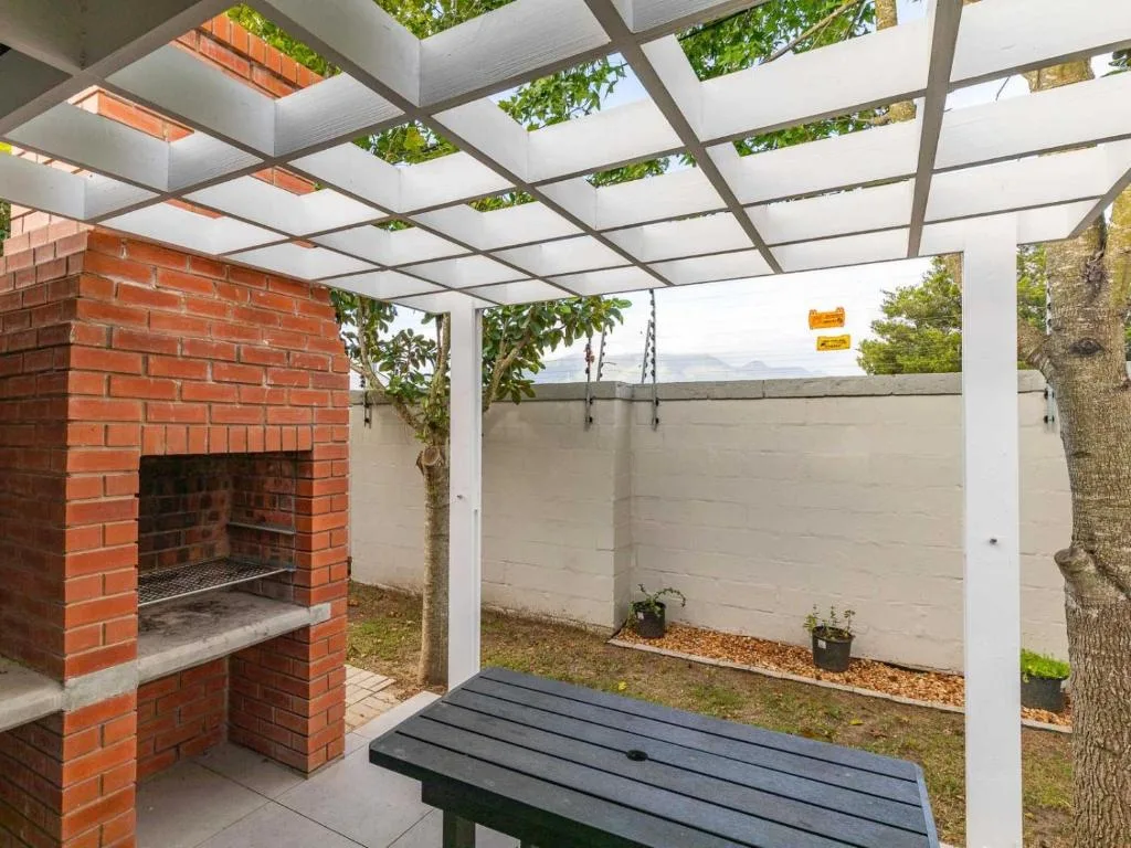 Covered patio with pergola, braai fireplace, and wooden seating area