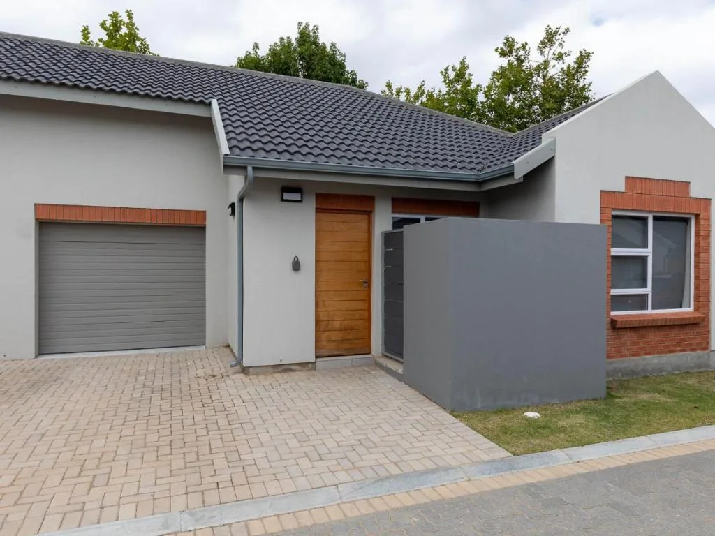 Modern white townhouse with dark roof, wooden door, and brick driveway entrance