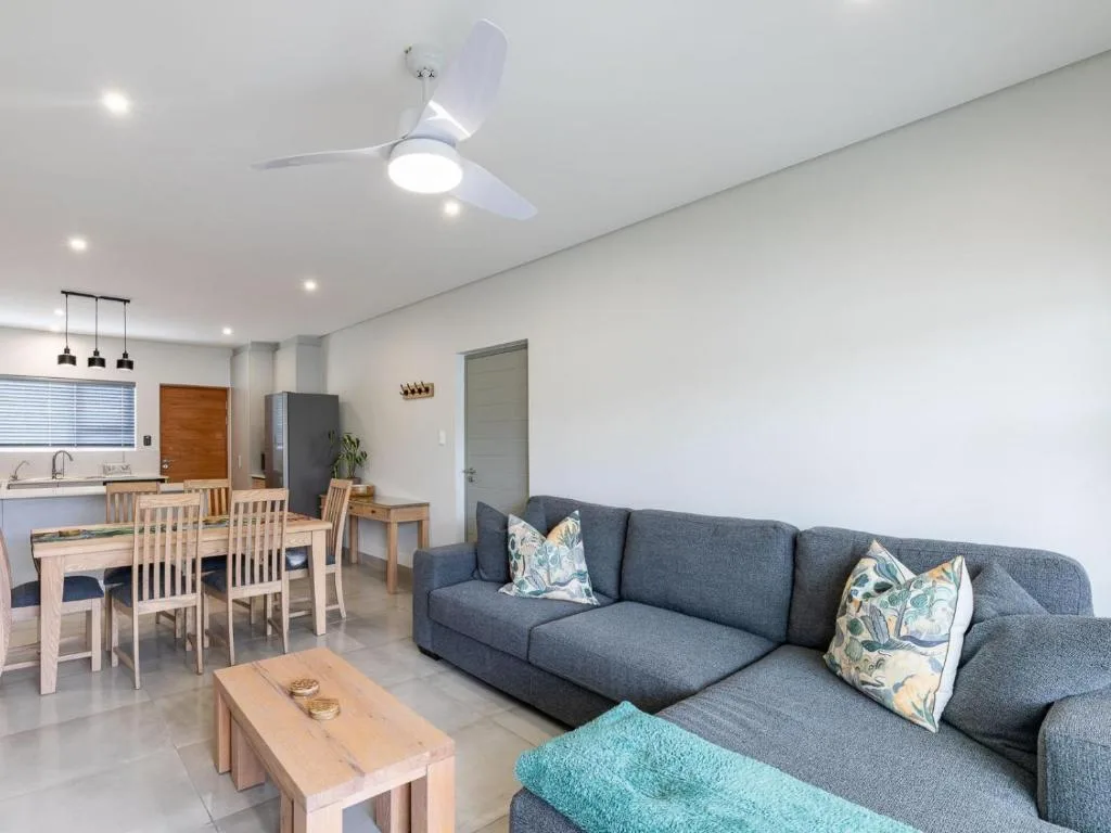 Modern open-plan lounge with gray sofa, wooden coffee table, and dining area beyond