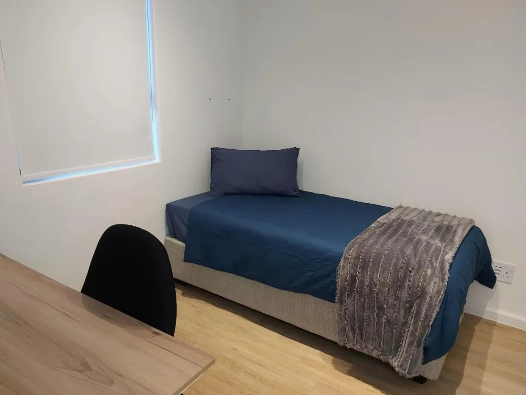 Single bed with navy bedding and grey throw blanket in bright room