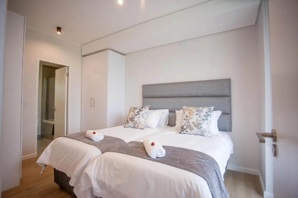 Modern bedroom with twin beds, gray upholstered headboard, and en-suite bathroom access