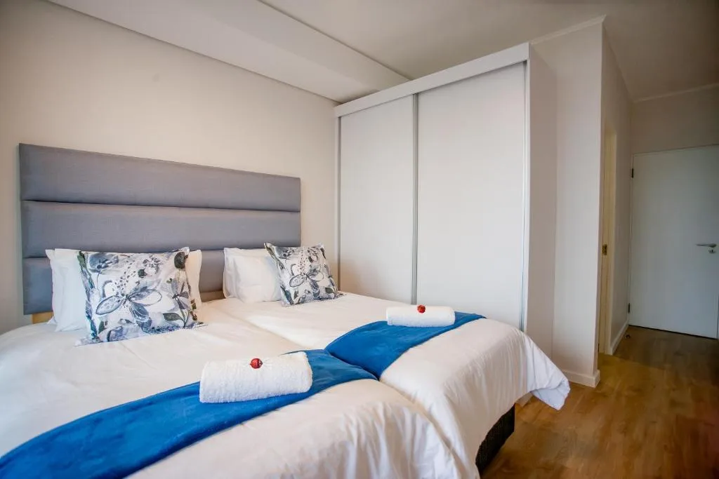 Twin beds with white linens, blue throws, and decorative pillows in bright bedroom