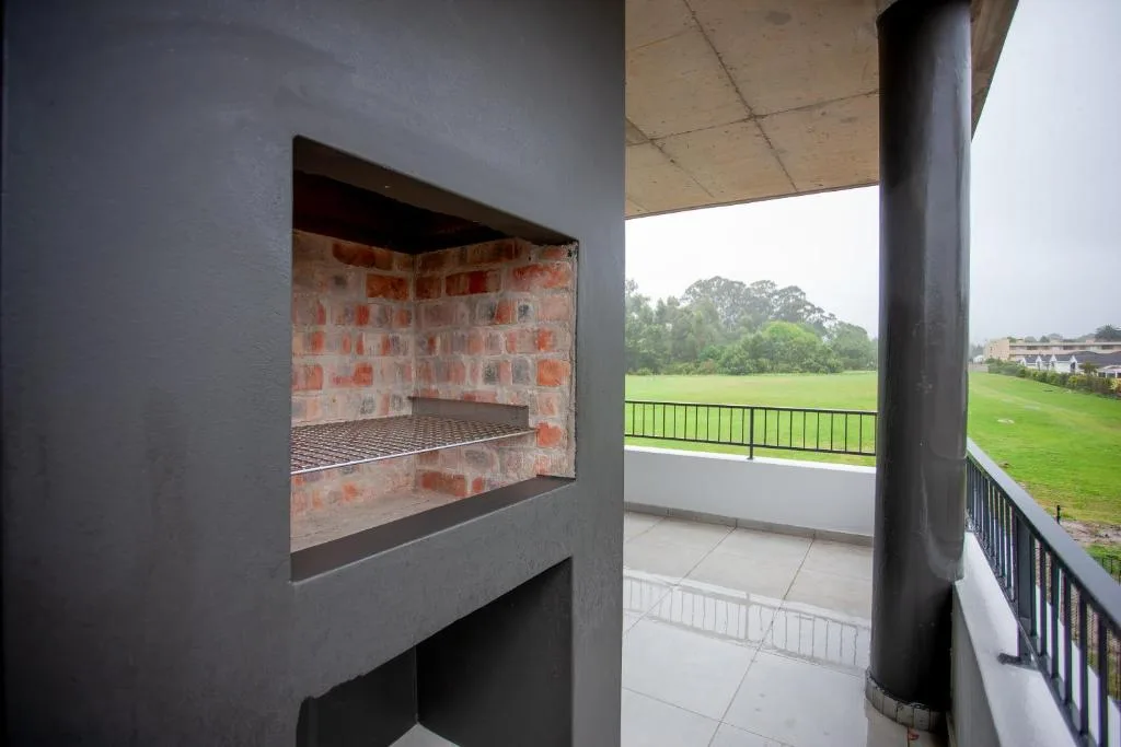 Covered outdoor deck with braai fireplace overlooking green fields and landscape