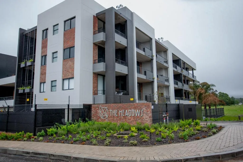 Modern multi-story apartment building with brick and white facade, entrance gardens