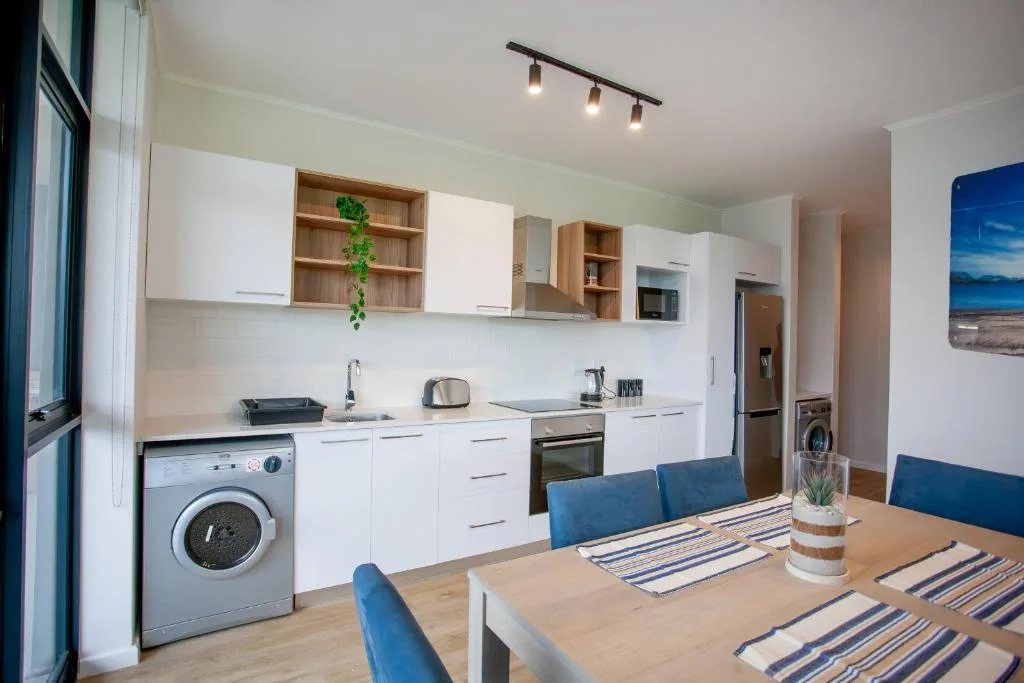 Modern open-plan kitchen with white cabinetry, stainless steel appliances, and dining table