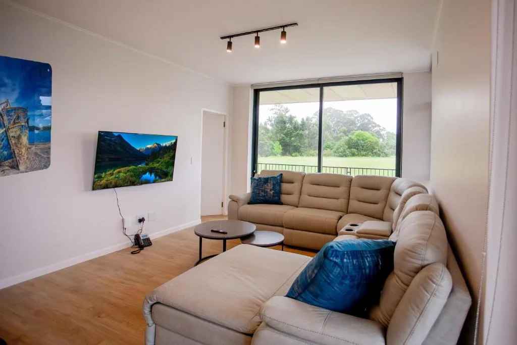 Spacious lounge with beige sectional sofa, TV, and large windows overlooking garden landscape