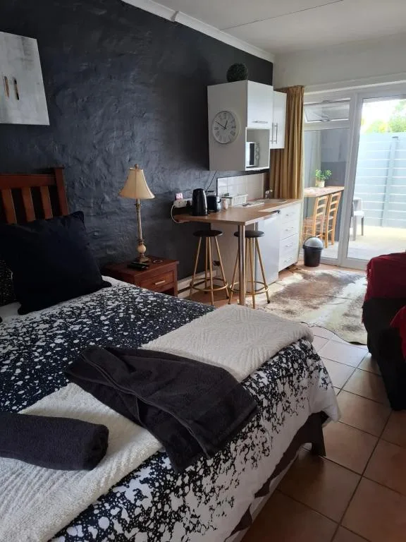 Modern bedroom with double bed, kitchenette, dark feature wall, and patio access