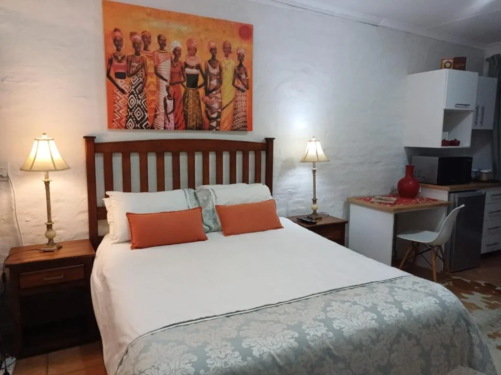 Bedroom with wooden bed frame, white linens, orange accent pillows, and bedside lamps