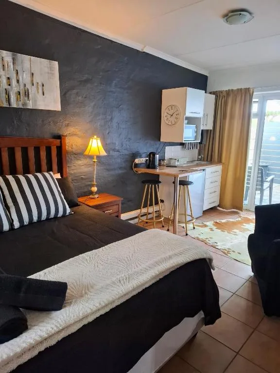 Modern bedroom with dark accent wall, wooden bed, and kitchenette area
