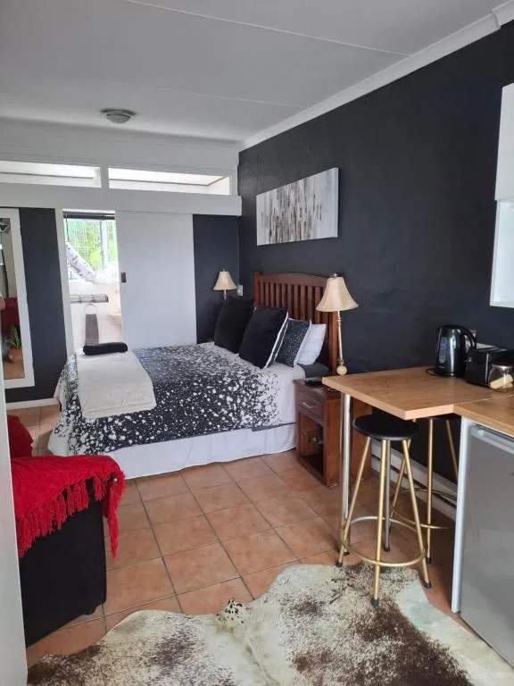 Modern bedroom with dark accent wall, queen bed, wooden desk, and ambient lighting