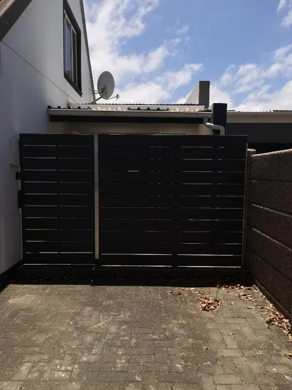 Modern black driveway gates with white building facade and satellite dish