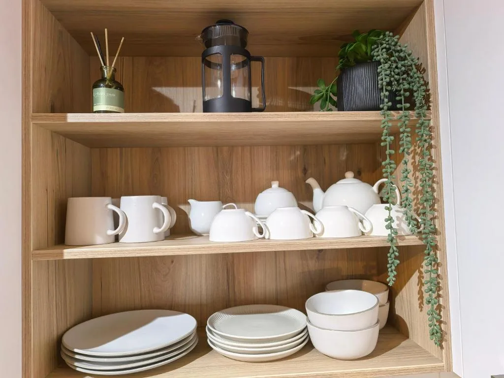 Open wooden shelving displaying white dishware, teapots, and decorative plants