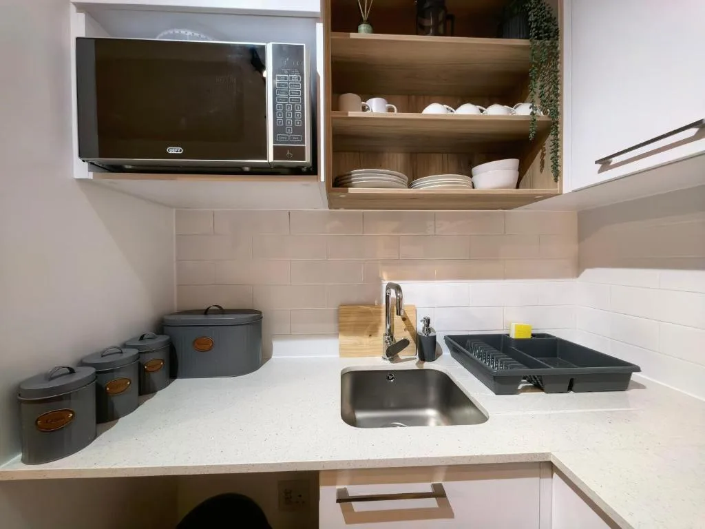 Modern kitchen with microwave, sink, white countertop, and wooden open shelving
