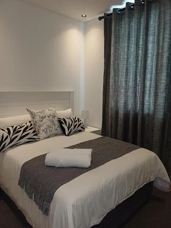 Modern bedroom with white headboard, patterned pillows, and grey curtains