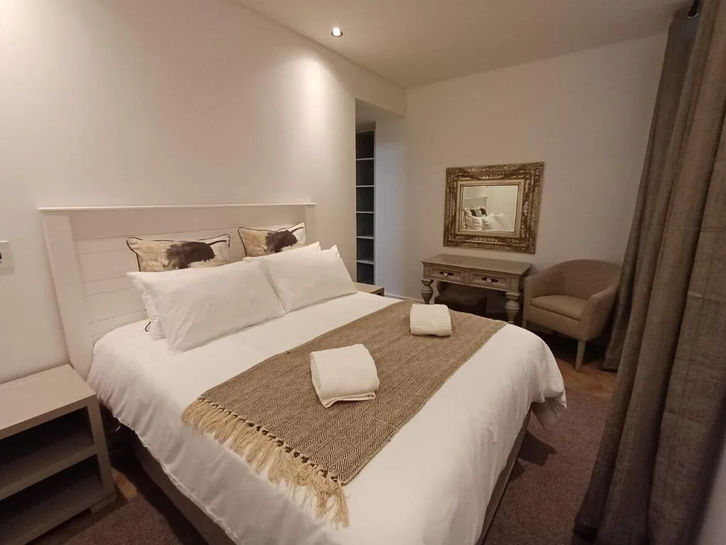 Spacious bedroom with white bedding, decorative pillows, and neutral furnishings