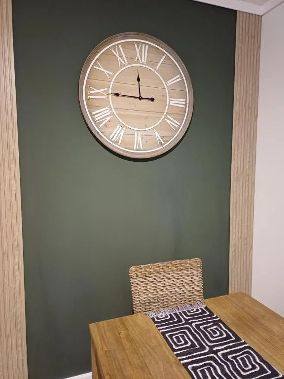 Wooden wall clock with Roman numerals above a dining table