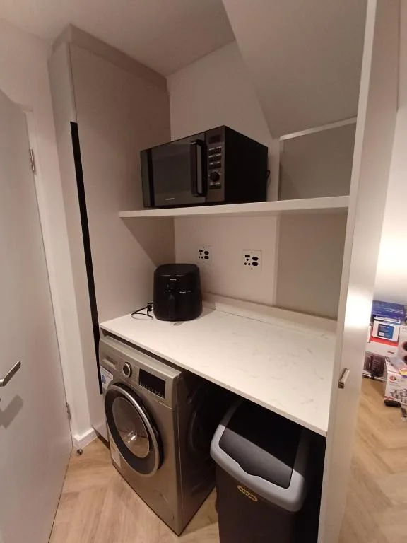 Compact laundry closet with washer, dryer, microwave, and storage shelves