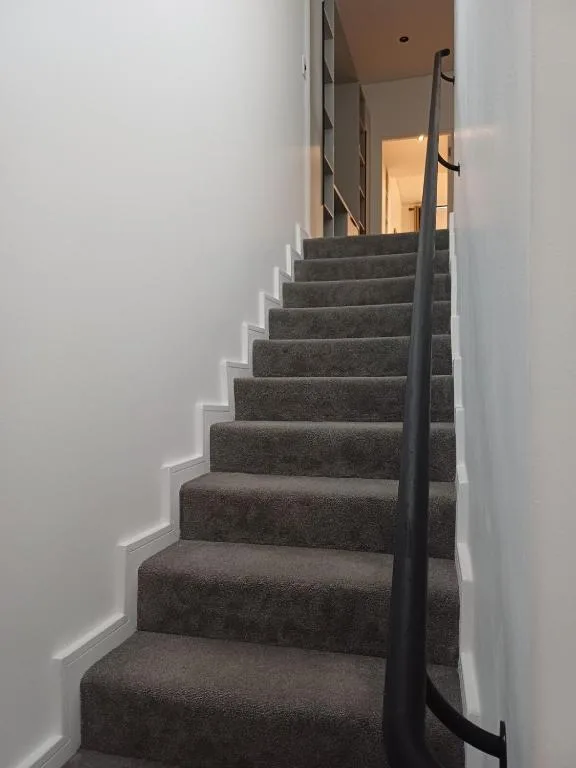 Interior staircase with grey carpet and black metal handrail leading upward