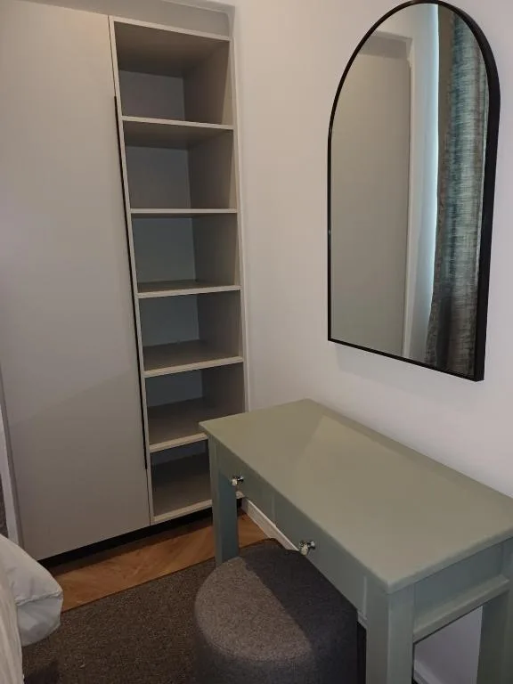 Bedroom vanity with mirror, shelving unit, and wooden floors