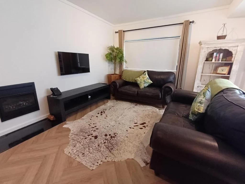 Spacious living room with dark leather sofas and wall-mounted television
