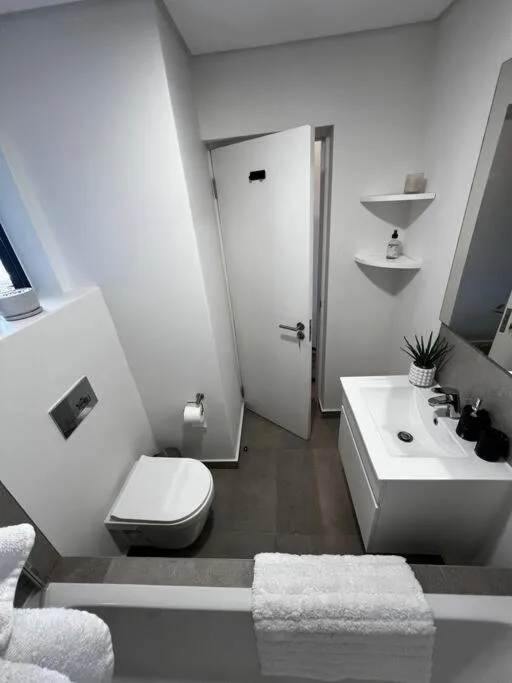 Modern bathroom with white vanity, toilet, corner shelves, and dark flooring
