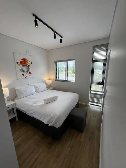 Bright modern bedroom with queen bed, white linens, and garden views through windows