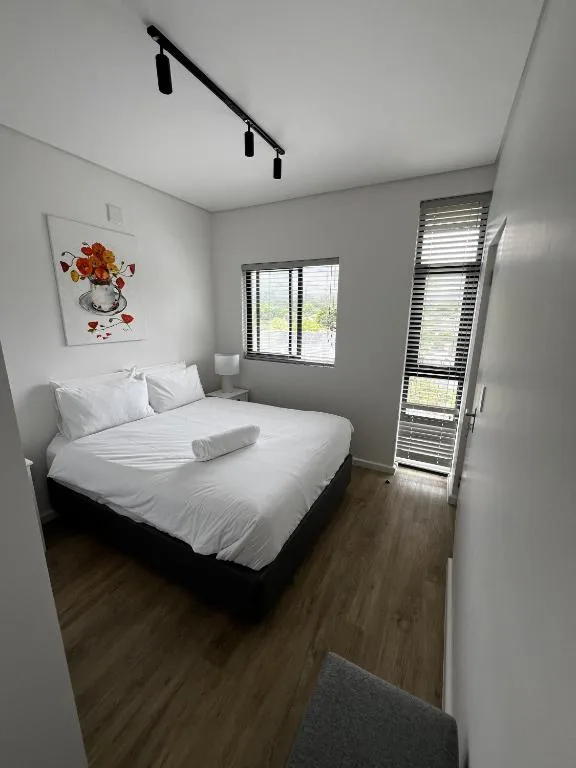 Bright modern bedroom with queen bed, white linens, and garden views through windows