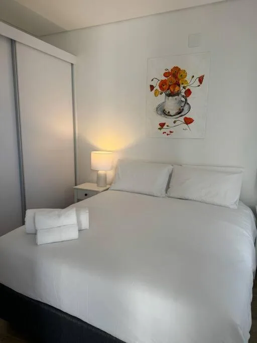 Bright bedroom with white bedding, mirror, and floral artwork on wall