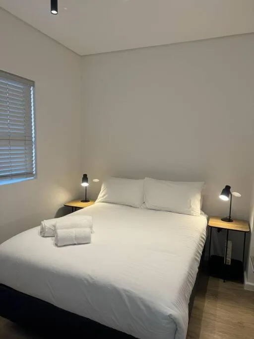 Bright modern bedroom with white bedding, twin bedside lamps, and window view