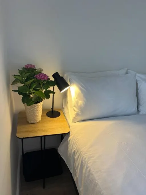 Bright bedroom with white pillows, bedside table, purple flowers, reading lamp