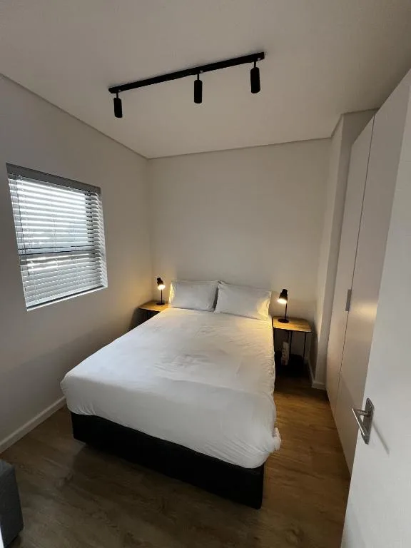 Bright bedroom with white duvet, bedside lamps, and natural light from window