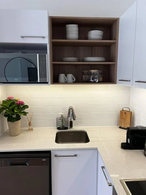 Modern kitchen with white cabinetry, microwave, sink, and open shelving with dishware