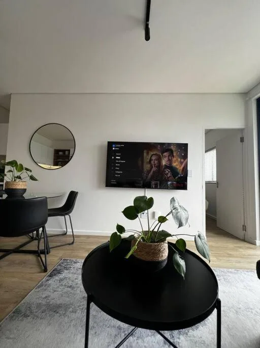 Modern living room with wall-mounted TV, round mirror, and potted plant on black table