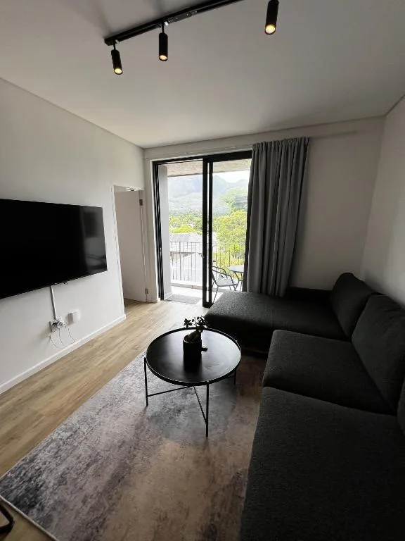 Modern lounge with black sofa, TV, and mountain views through glass doors