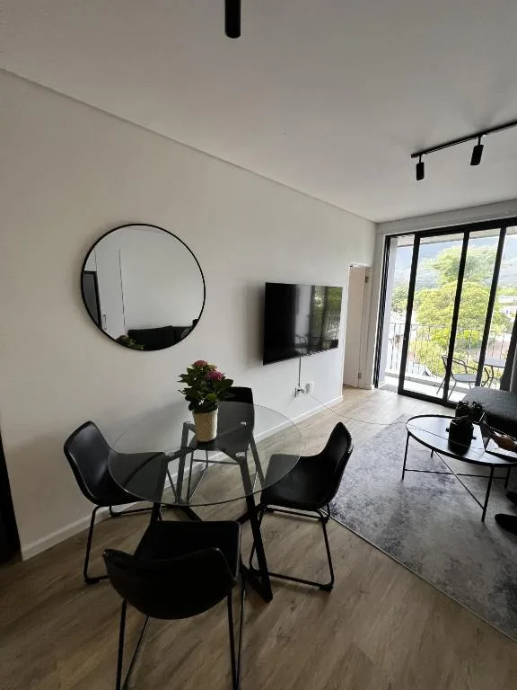Modern lounge with round mirror, dining table, TV, and garden views through glass doors