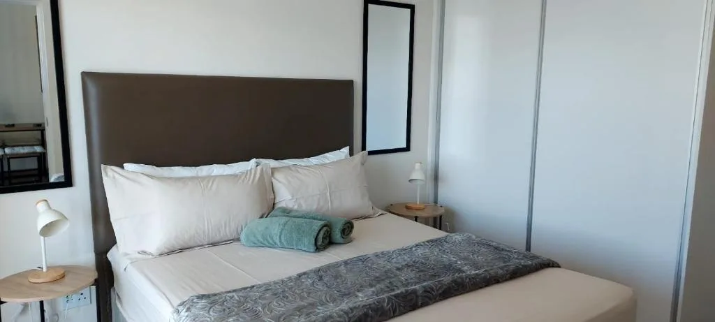 Modern bedroom with brown headboard, white pillows, and teal towels