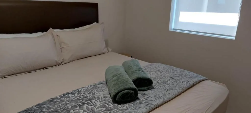 Neatly made bed with fresh linens and rolled towels, bright window