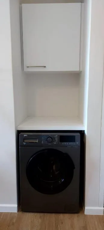 Black washing machine in built-in alcove with white cabinet above