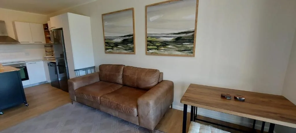 Brown leather sofa in open-plan lounge with landscape artwork on walls