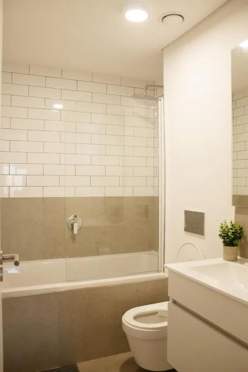Modern bathroom with subway tile shower, white vanity, and toilet
