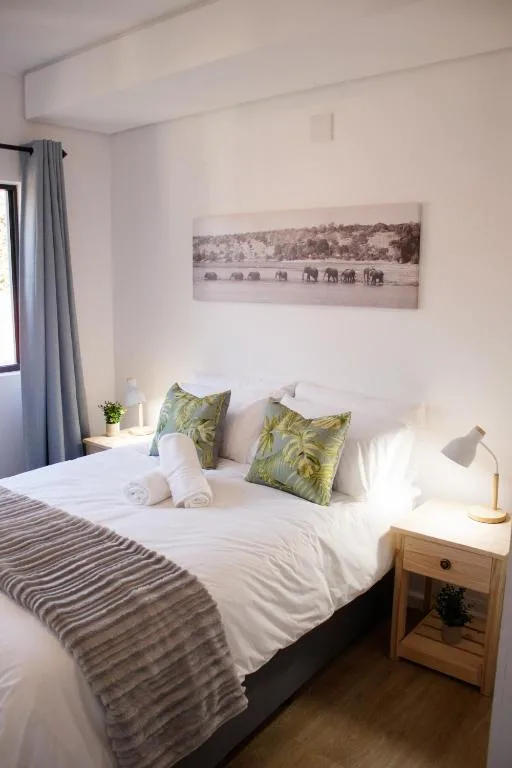 Bright bedroom with double bed, green cushions, wooden nightstand, and wall art