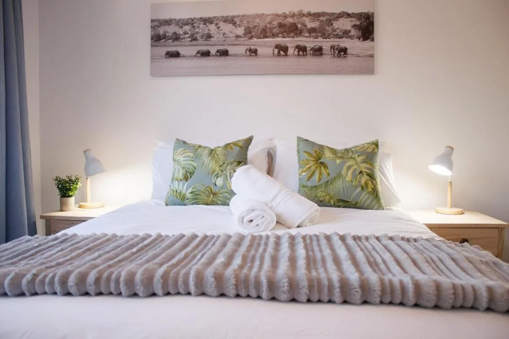 Spacious bedroom with crisp white bedding, tropical patterned pillows, and elephant artwork