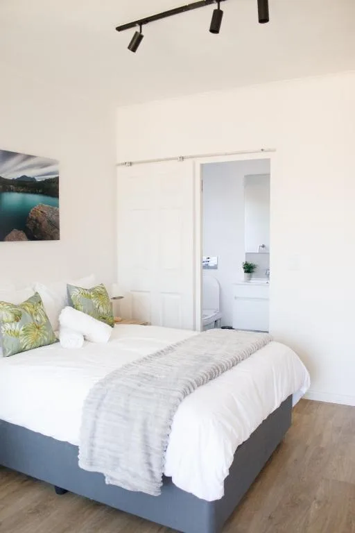 Bright bedroom with queen bed, green pillows, and ensuite bathroom access