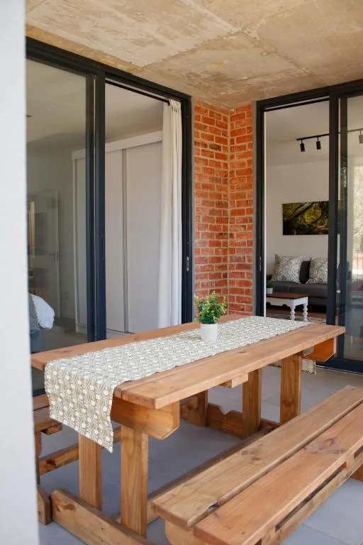 Wooden outdoor dining table on covered deck with brick interior visible