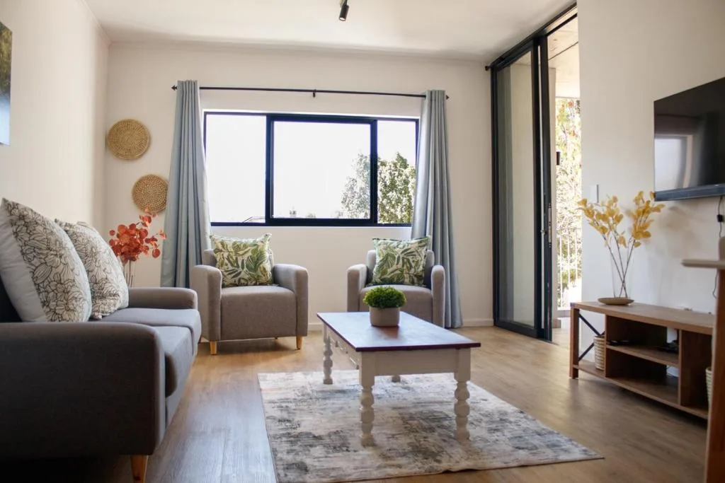 Bright living room with comfortable seating, coffee table, and garden views through large windows
